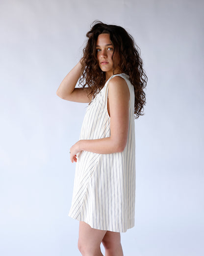 Cream sleeveless mini dress with thin vertical stripes, relaxed fit, modeled sideways