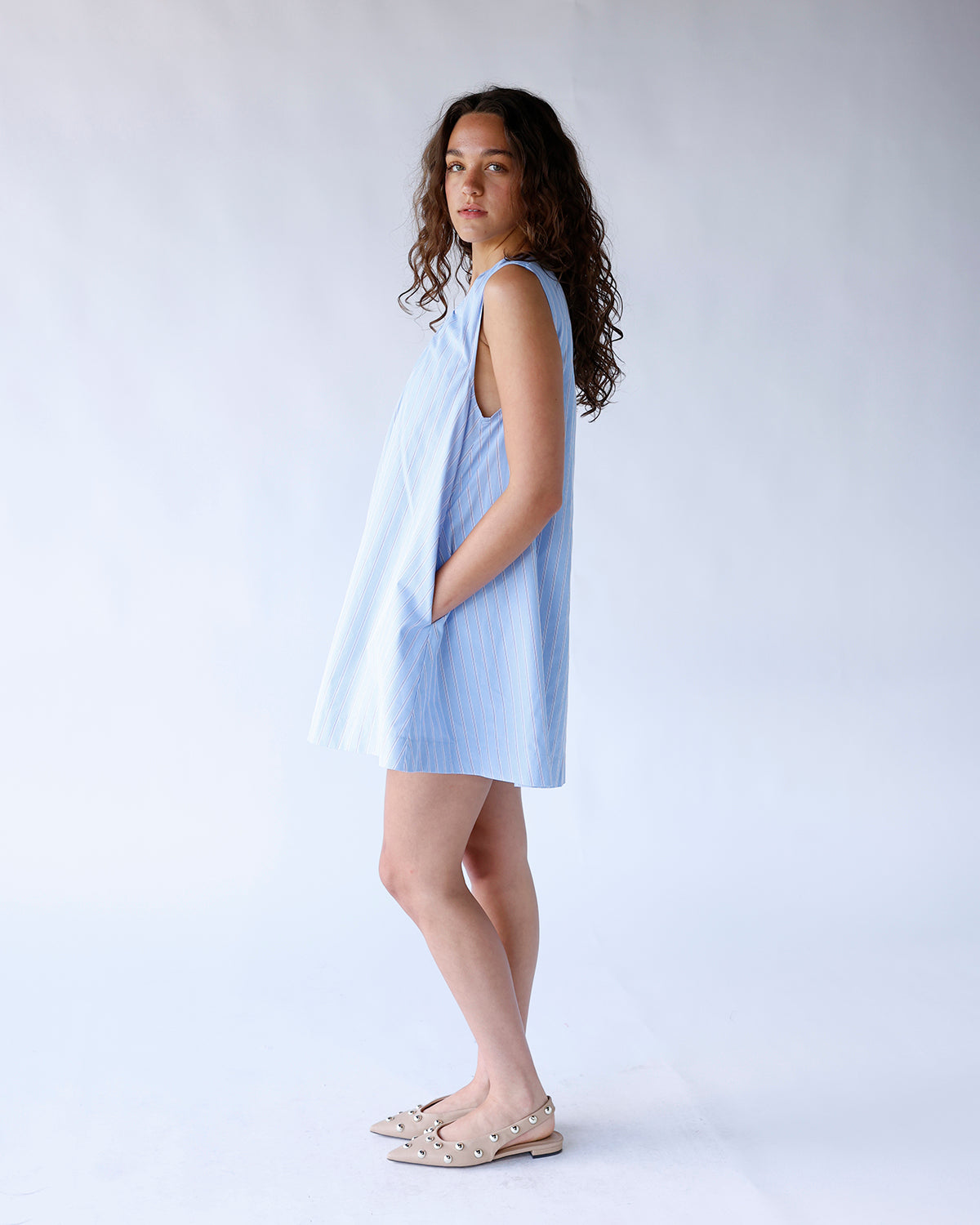 Light blue striped sleeveless mini swing dress with side pockets, worn with beige studded flats