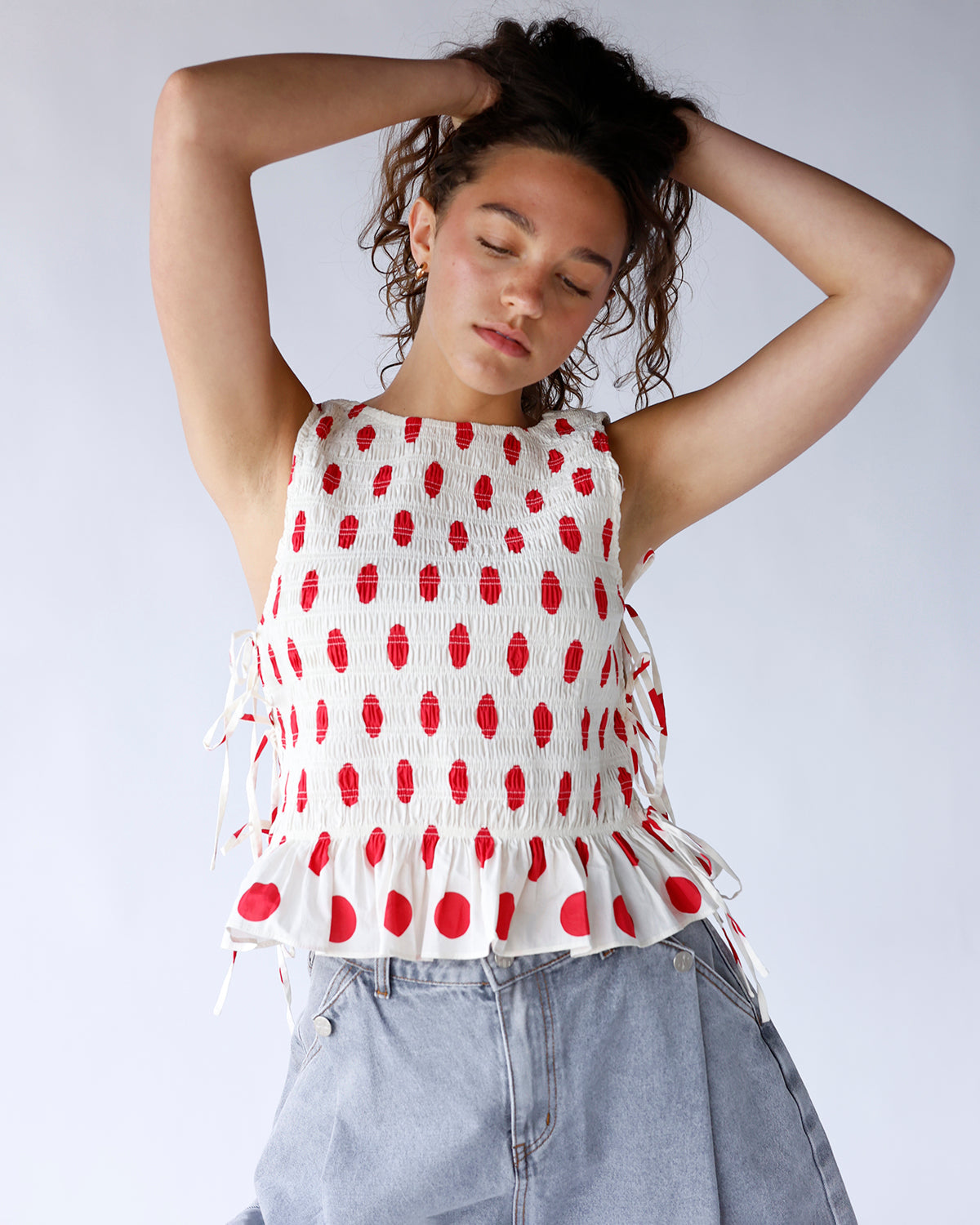 White sleeveless peplum blouse with red polka dots, side tie detail, and scoop back neckline. A playful, feminine top perfect for summer and casual styling.