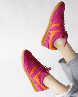 Fuchsia pink sneakers with orange stripe accents and gum rubber sole, lace-up style