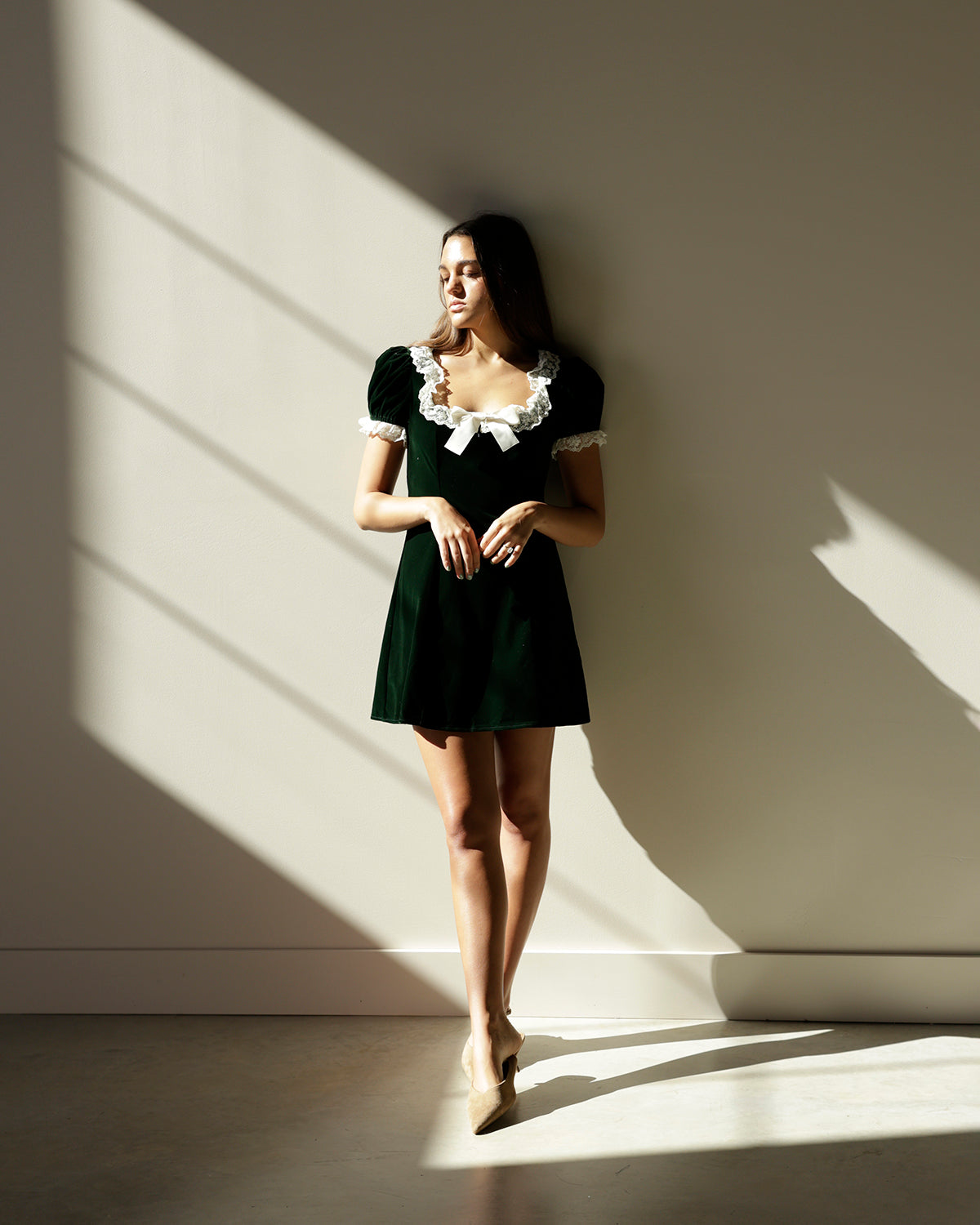 girl wearing green velvet velour baby doll dress with lace detailing and a bow wearing kitten heals and hair down 