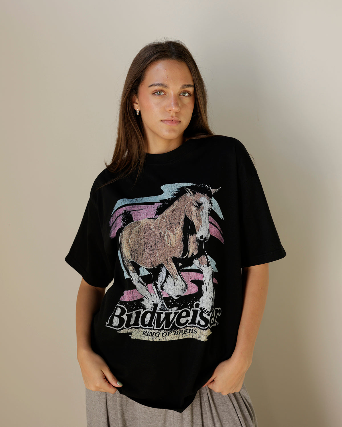 women's black oversized budweiser graphic t-shirt featuring a distressed galloping horse illustration, faded pink and blue accents, and vintage king of beers lettering.