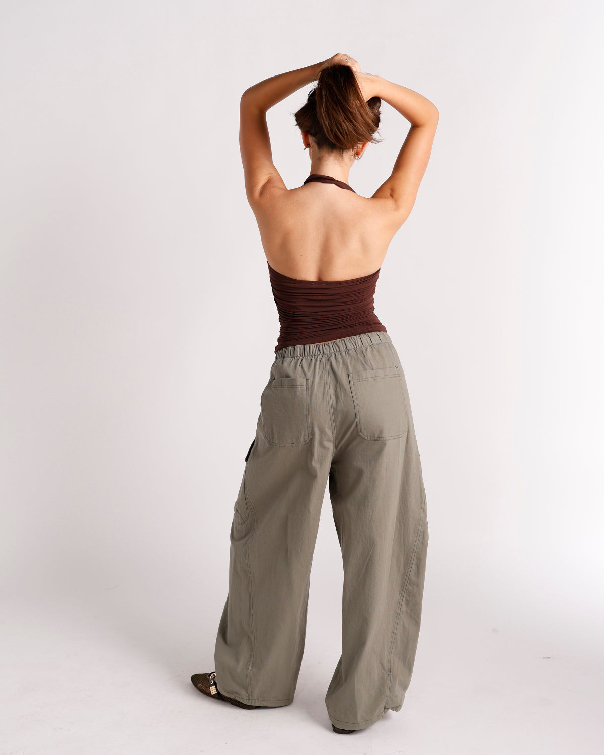 Dark brown backless halter top with ruched fabric, worn with olive wide-leg pants