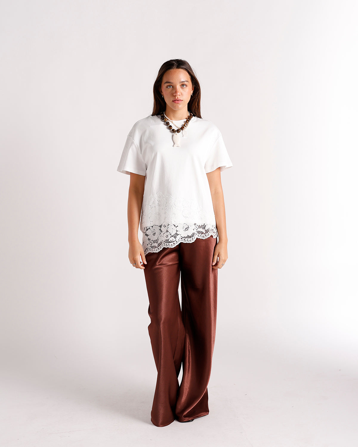 White lace-hem short sleeve top with brown wide-leg satin trousers and statement necklace
