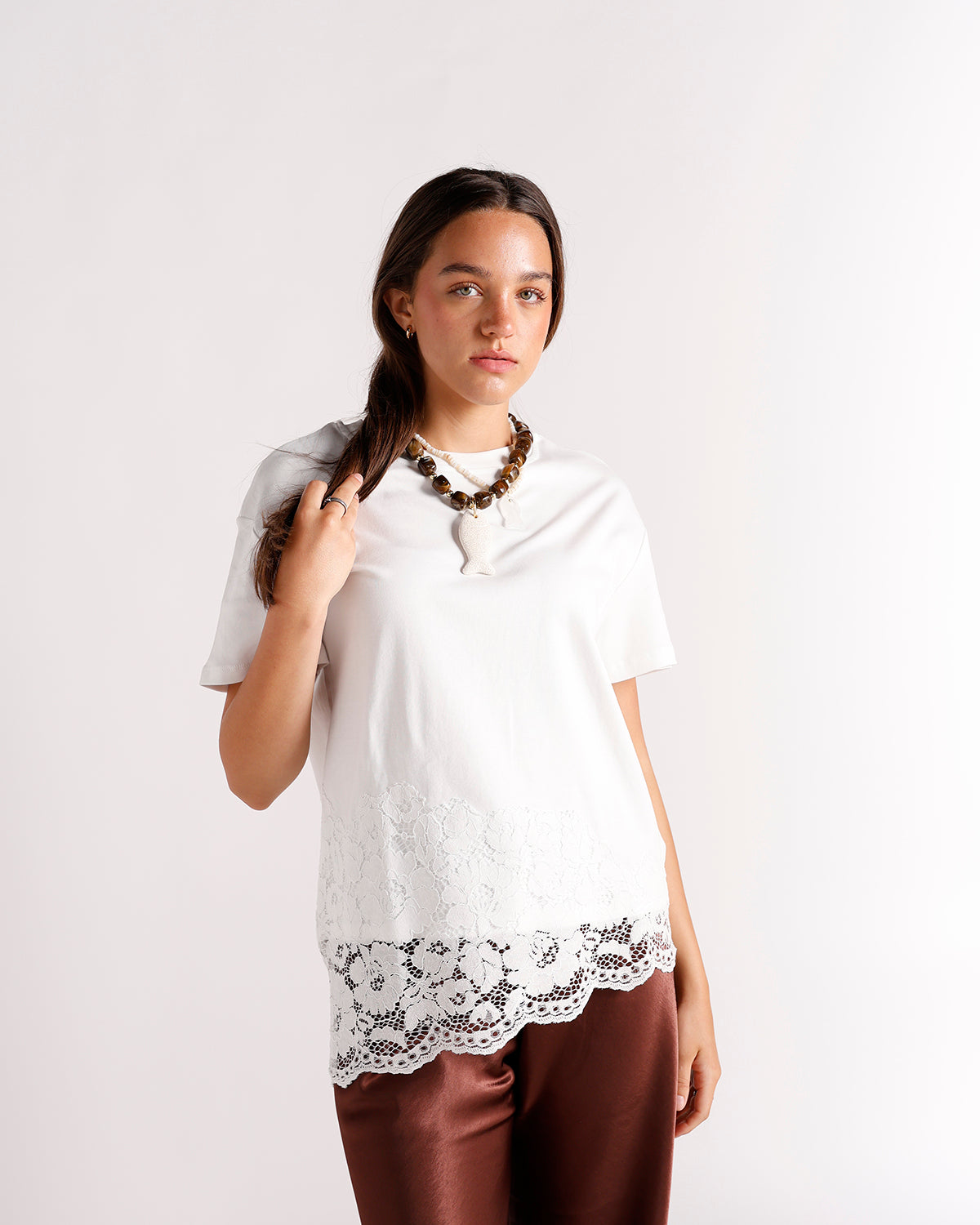 White lace-hem short-sleeve top with brown beaded necklace and rust satin pants