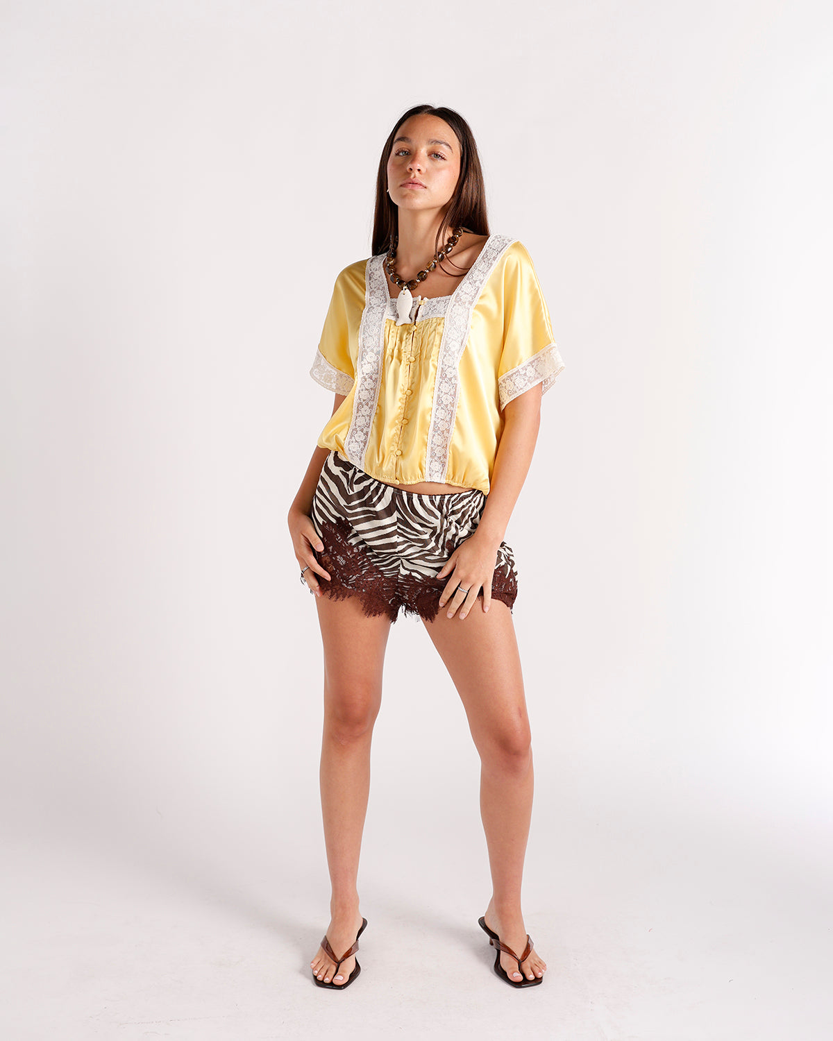 Yellow satin crop top with white lace trim, short sleeves, and button front detail