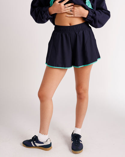 Navy blue athletic shorts with teal trim and elastic waistband, worn with sneakers