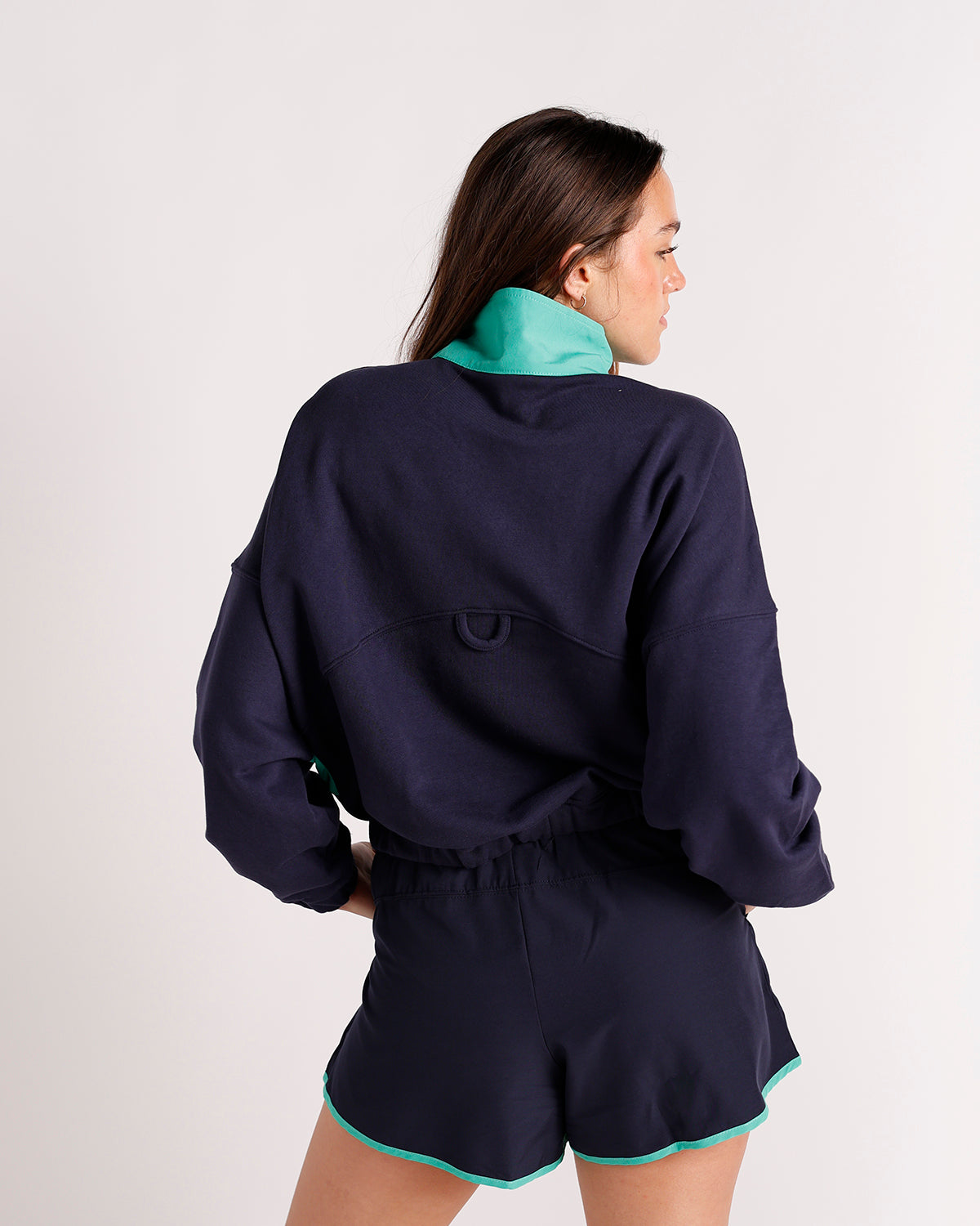 Women's navy quarter-zip sweatshirt with teal collar and matching navy shorts, back view.