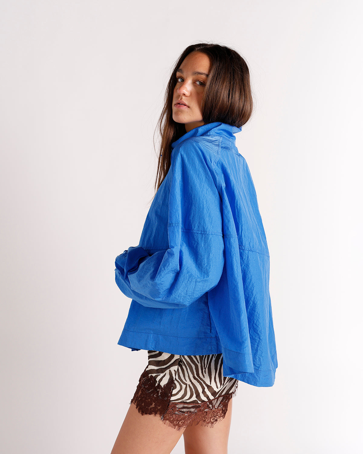 Oversized blue windbreaker jacket with wide sleeves, side view on model