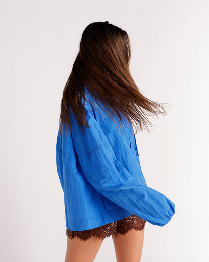Bright blue oversized windbreaker jacket with balloon sleeves, worn over brown lace shorts.
