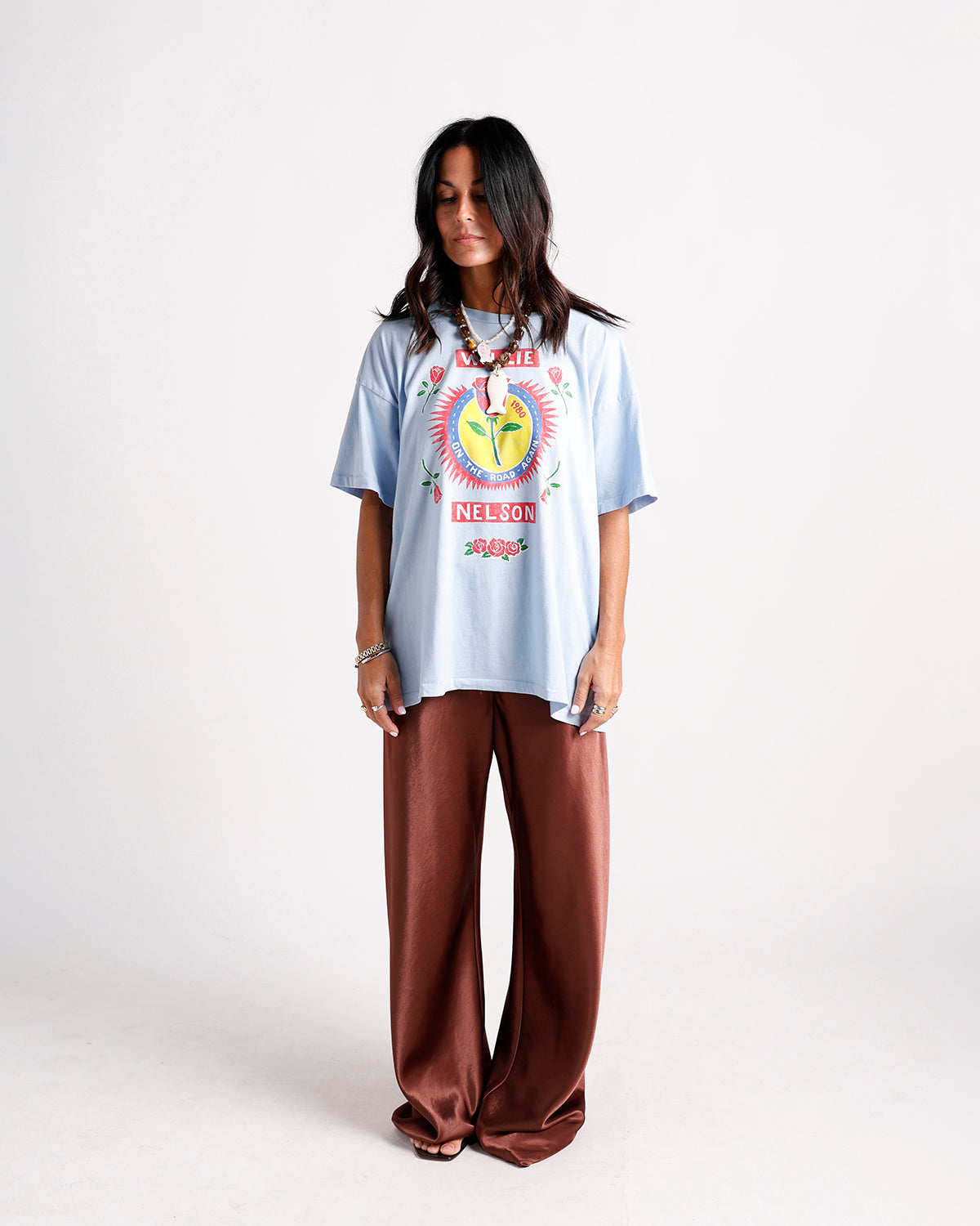 Oversized light blue graphic tee with brown wide-leg satin pants and beaded necklace