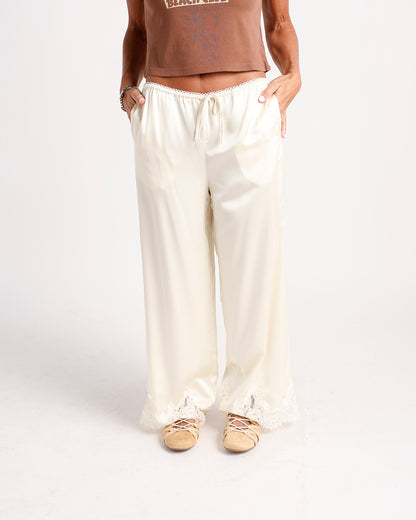 Cream wide-leg satin pants with lace trim at waist and hem, drawstring