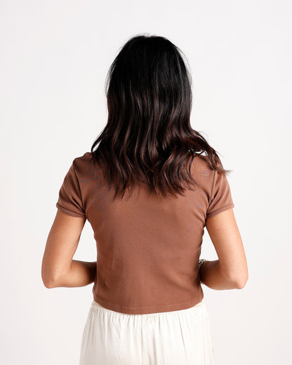 Back view of brown ribbed crop tee with short sleeves paired with white skirt
