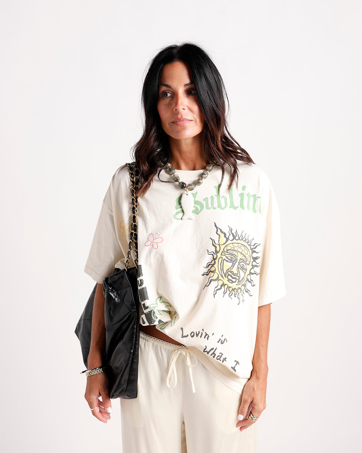 Cream oversized graphic tee with sun print and green gothic lettering worn with cream joggers