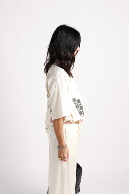 Cream oversized graphic tee with doodle prints, worn with cream wide-leg pants, side view