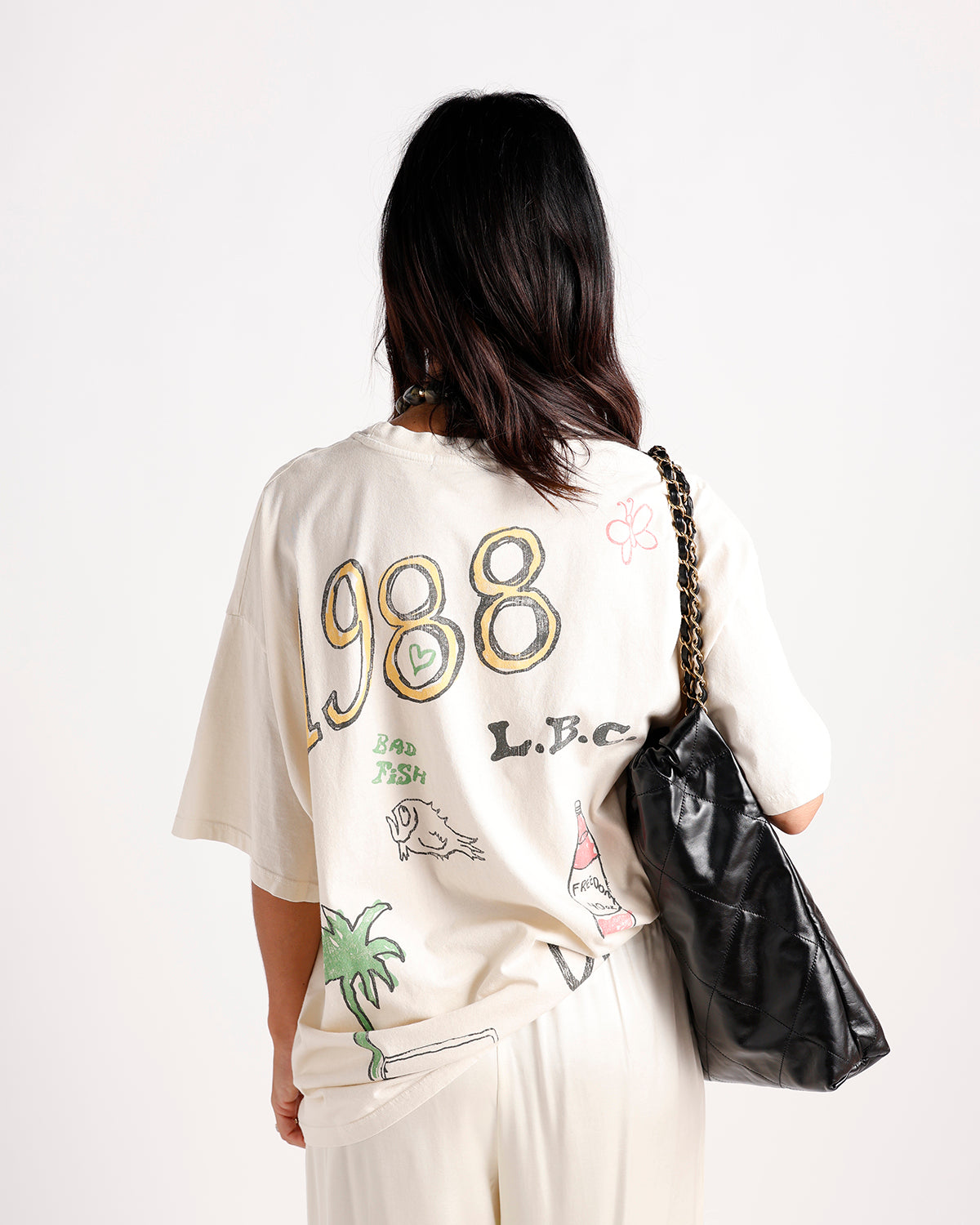Cream oversized graphic tee with 1988 L.B.C. print, worn from behind