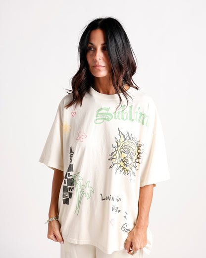 Oversized cream graphic tee with sun, palm trees, and colorful doodle prints