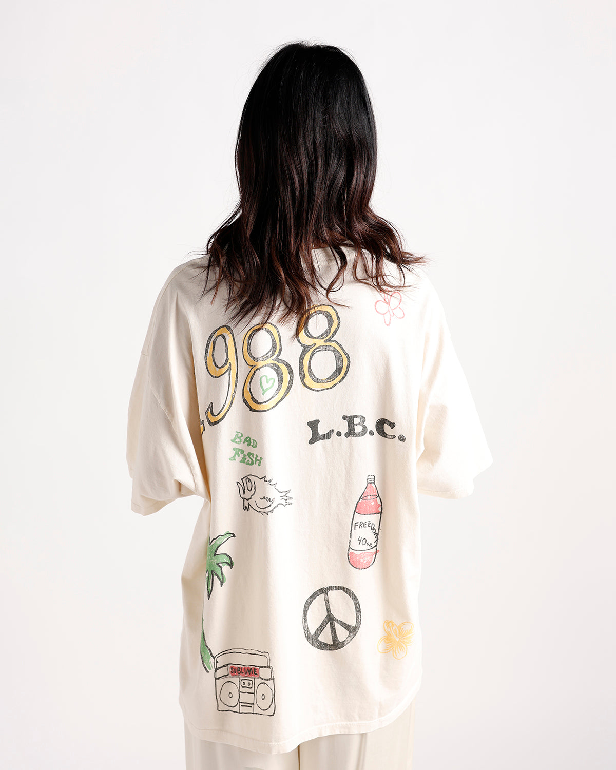 Oversized cream graphic tee back view with 988, L.B.C., peace sign, palm tree prints