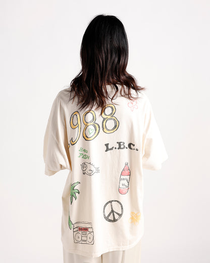Oversized cream graphic tee back view with 988, L.B.C., peace sign, palm tree prints