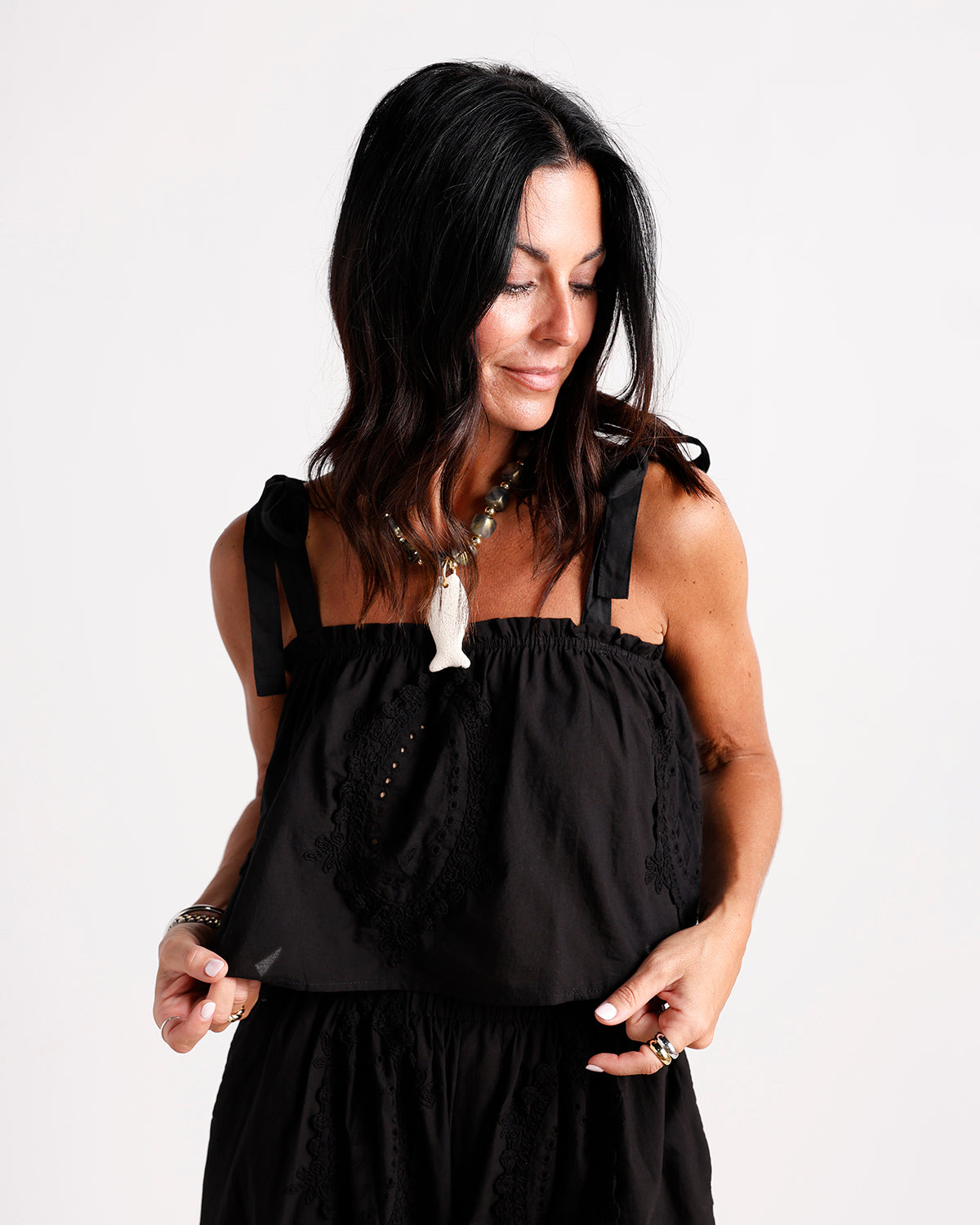 Black sleeveless top with tie straps, ruched neckline, and lace embroidery details