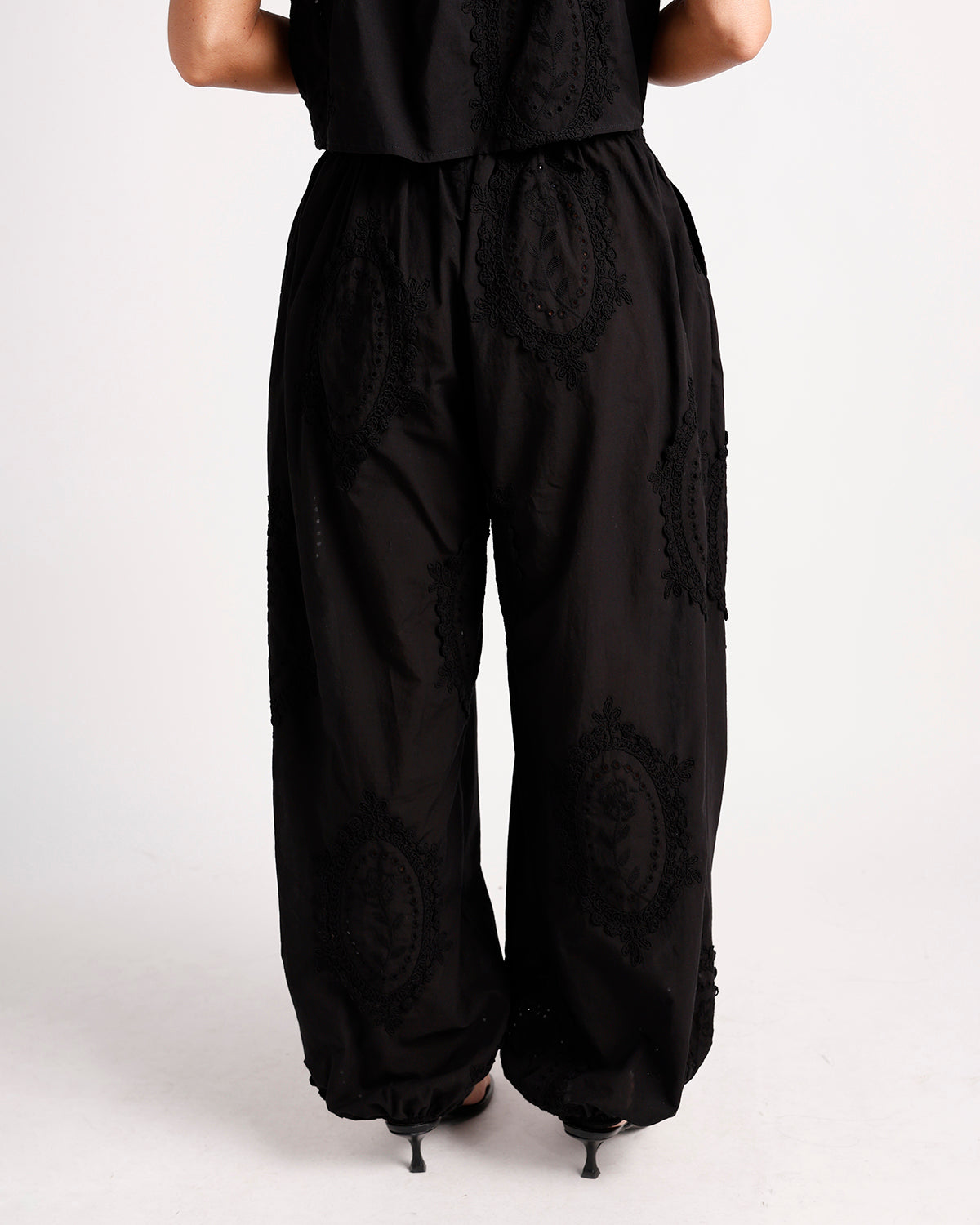 Black wide-leg pants with circular lace embroidery and elastic waistband, back view