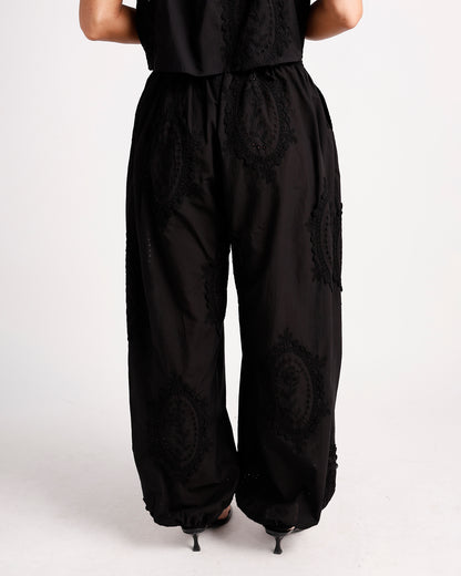 Black wide-leg pants with circular lace embroidery and elastic waistband, back view