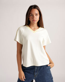 Cream v-neck tee with yellow contrast collar, short sleeves, paired with blue jeans.