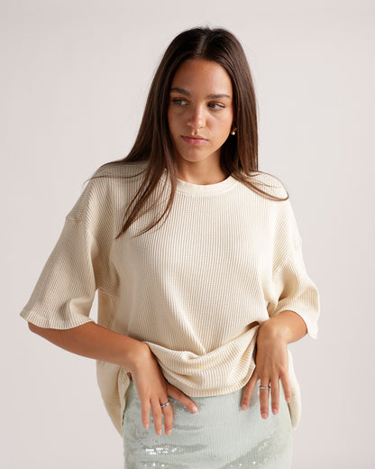 Cream ribbed knit short-sleeve tee with relaxed fit, worn with a sequin skirt.