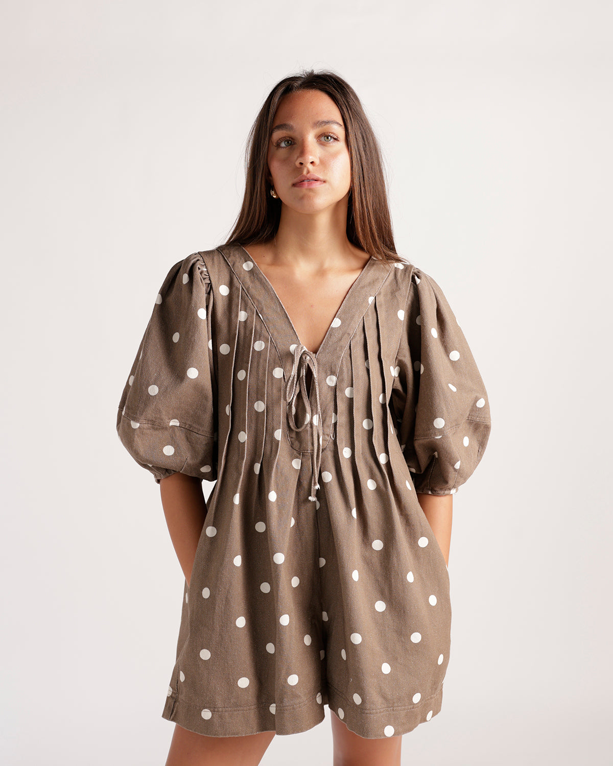Brown and white polka dot romper featuring a flattering tie-front detail, balloon sleeves, and an easy shorts silhouette. The perfect playful romper for brunch, vacations, weekend outings, and sunny-day style.
