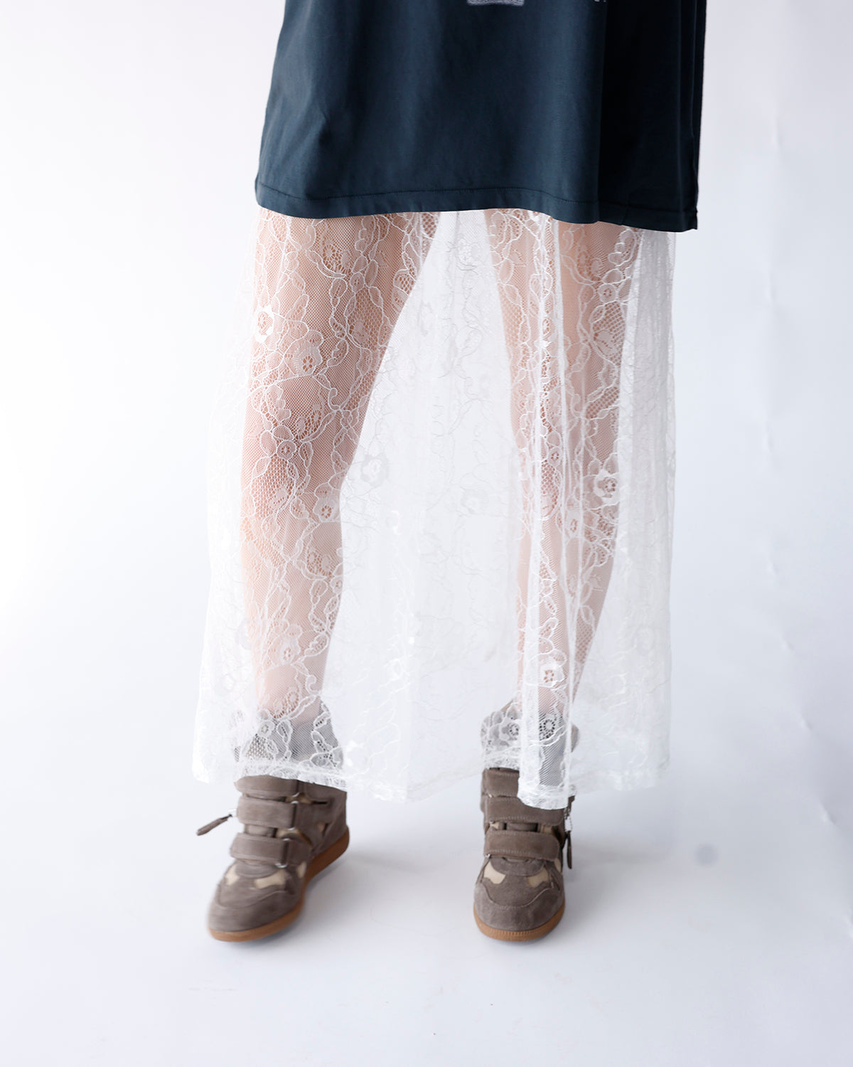 White floral lace sheer maxi skirt layered over dark top with sneakers