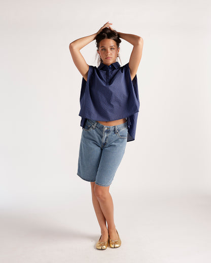 Medium wash baggy denim shorts, knee length, worn with navy striped top and gold flats.