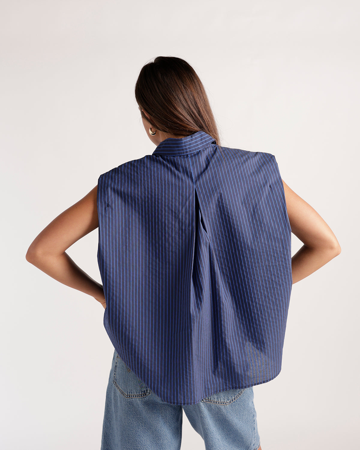 Sleeveless navy blue pinstripe button-up top with structured shoulders, back view