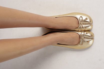 Gold metallic split-toe ballet flats with bow detail, worn on feet