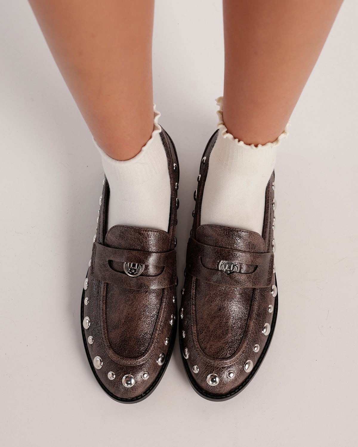 Dark taupe studded leather loafers worn with white frilly ankle socks, top view