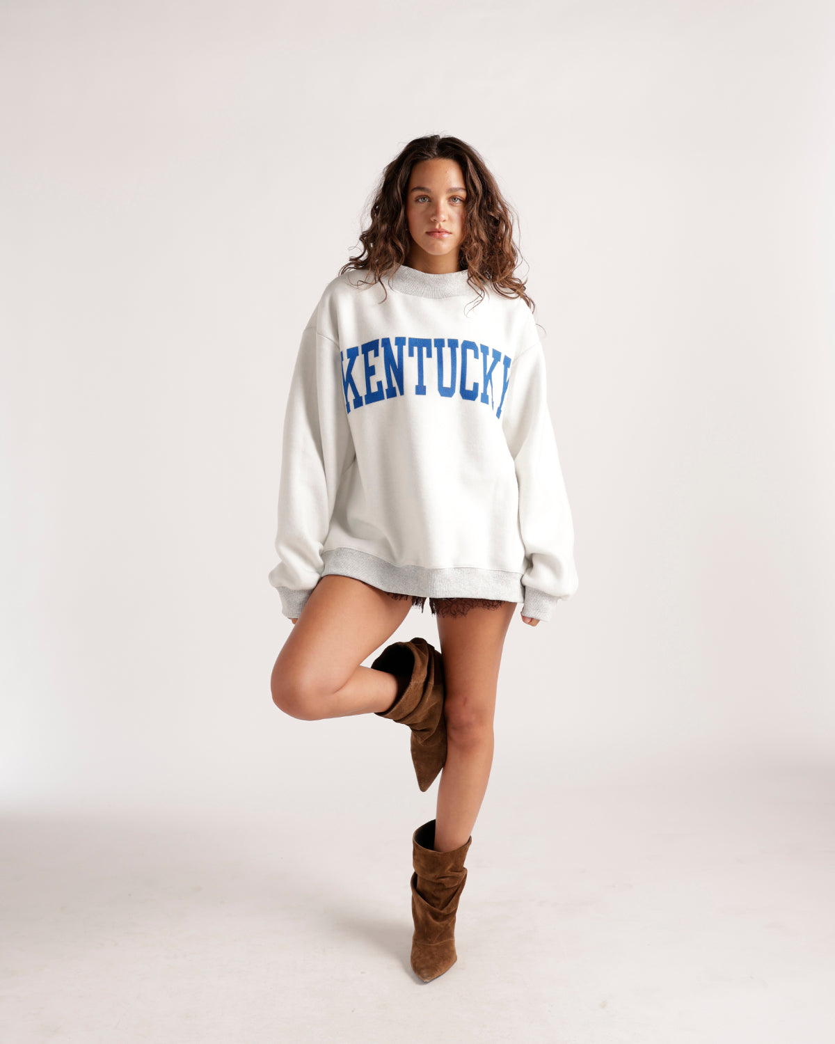 Oversized white Kentucky graphic crewneck sweatshirt styled with brown shorts and boots