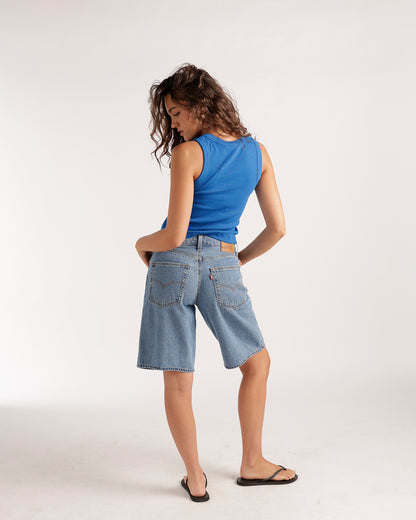 Baggy medium wash denim shorts with back pockets, worn with blue tank top
