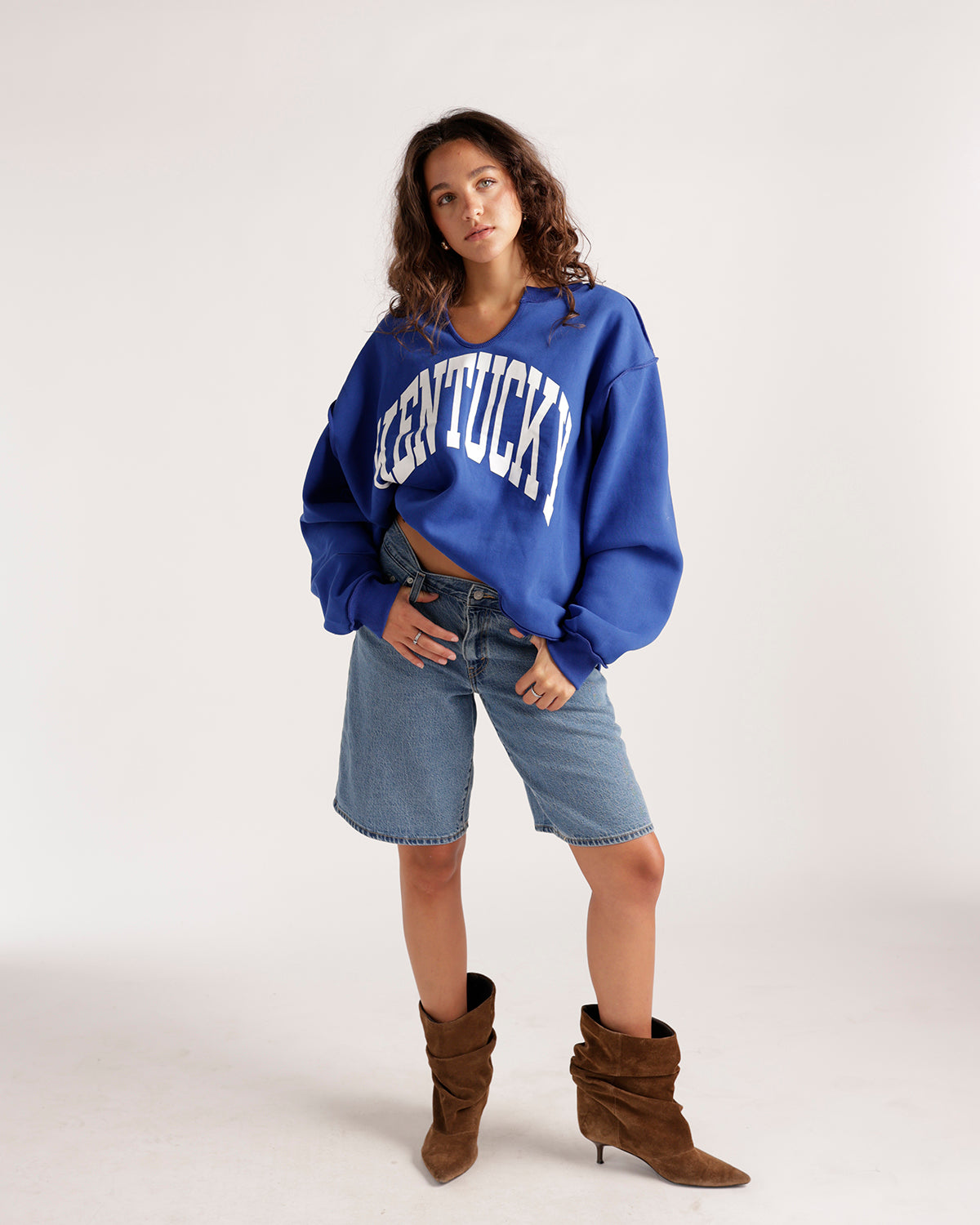 Medium wash baggy denim shorts with frayed hem, worn with blue sweatshirt and brown boots.