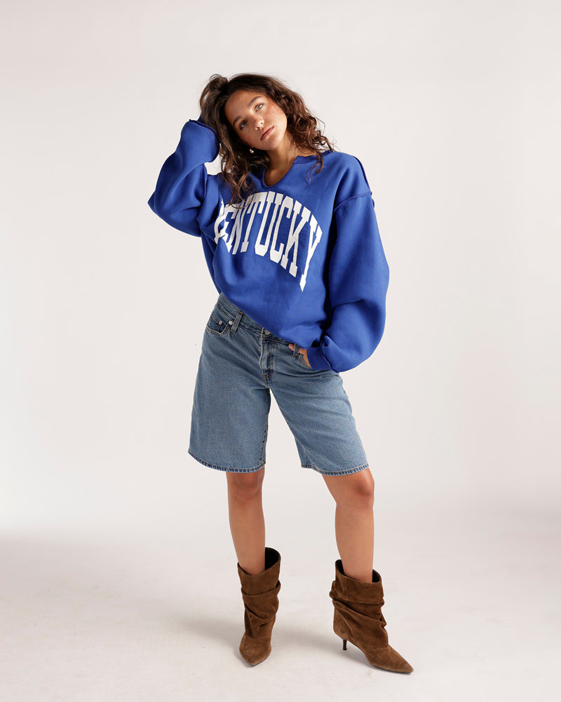 Oversized royal blue Kentucky split neck sweatshirt styled with denim shorts and brown boots