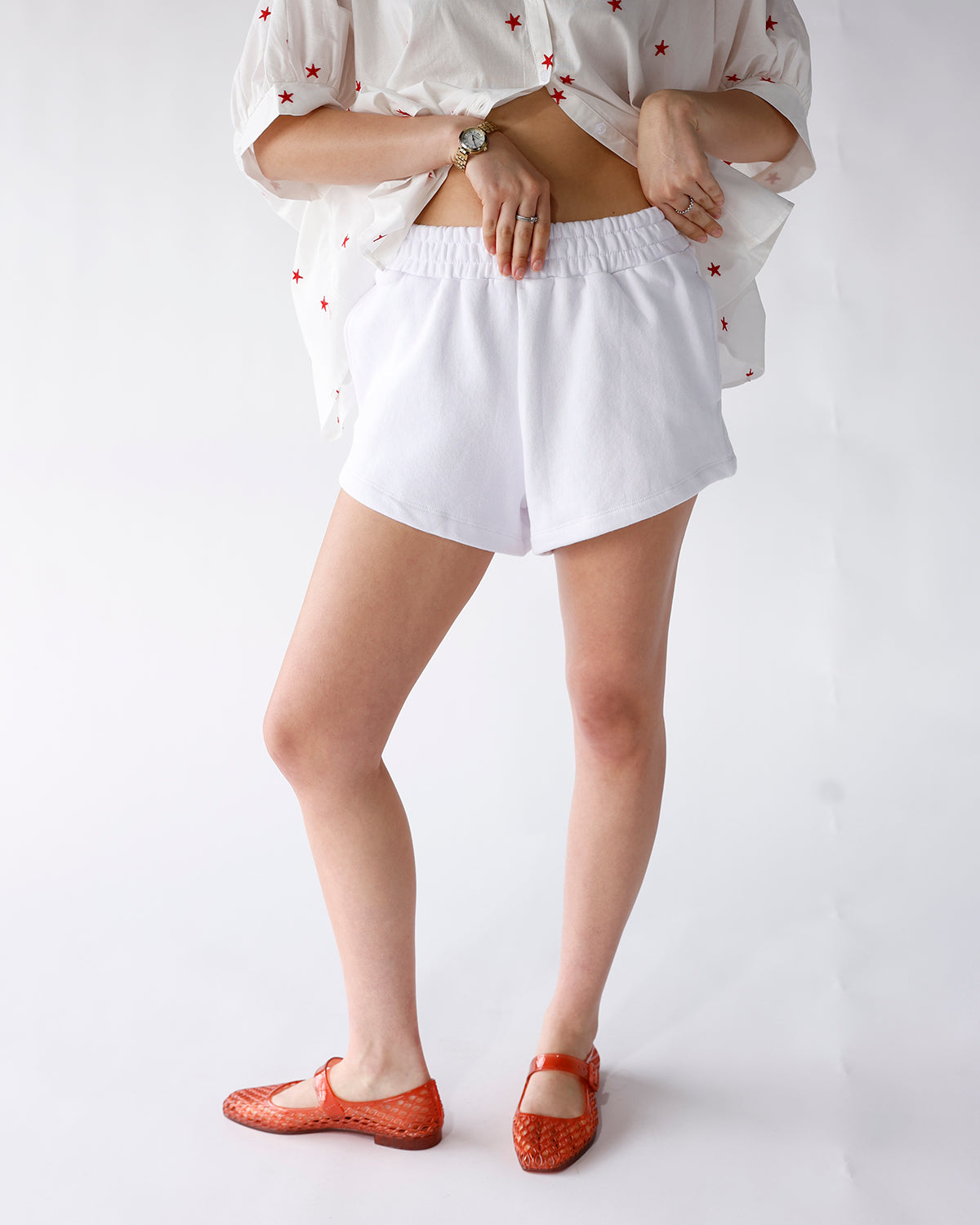 White elastic-waist terry shorts with curved hem, styled with star-print top