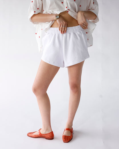 White elastic-waist terry shorts with curved hem, styled with star-print top