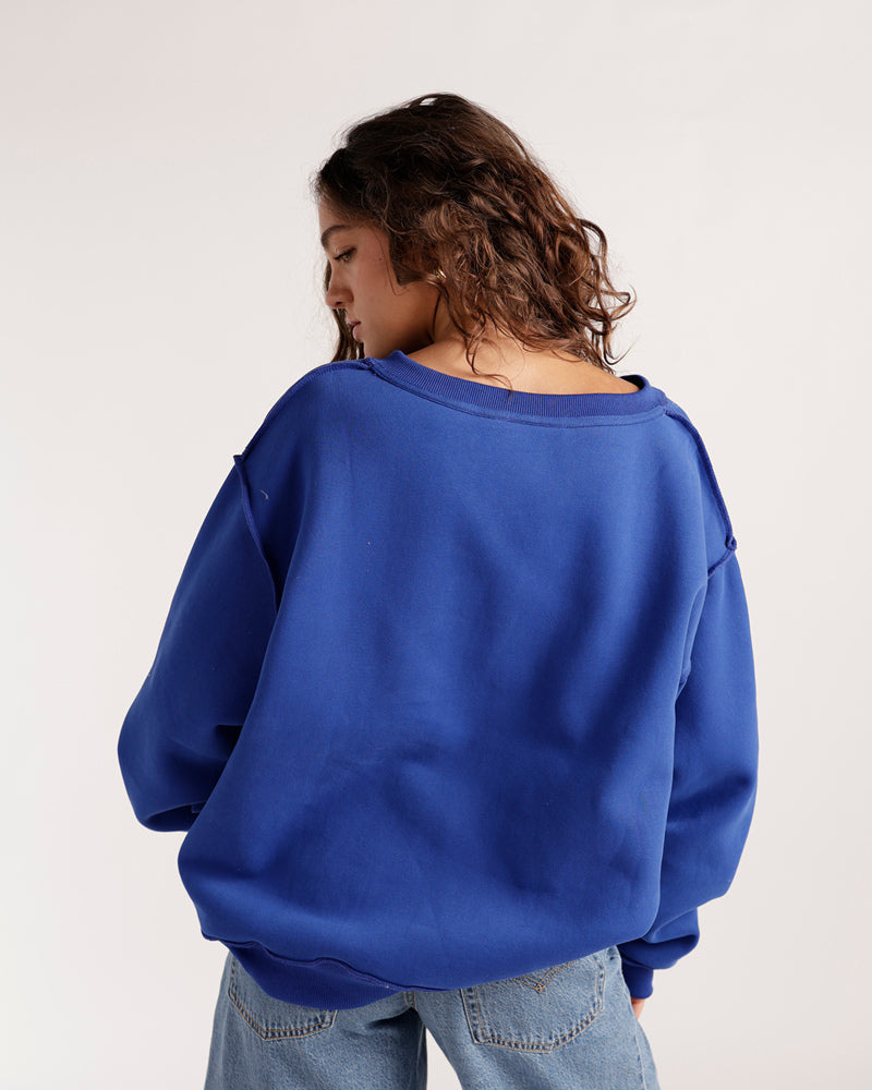 Oversized royal blue split neck reversible sweatshirt, back view, paired with jeans