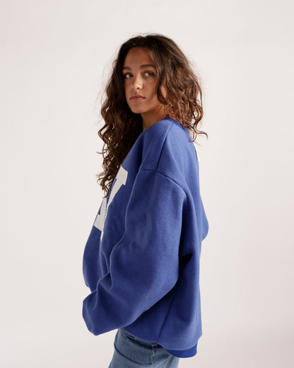 Oversized blue reversible sweatshirt with white graphic lettering, side profile view