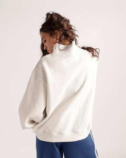 Oversized cream mock neck sweatshirt, back view, paired with blue track pants