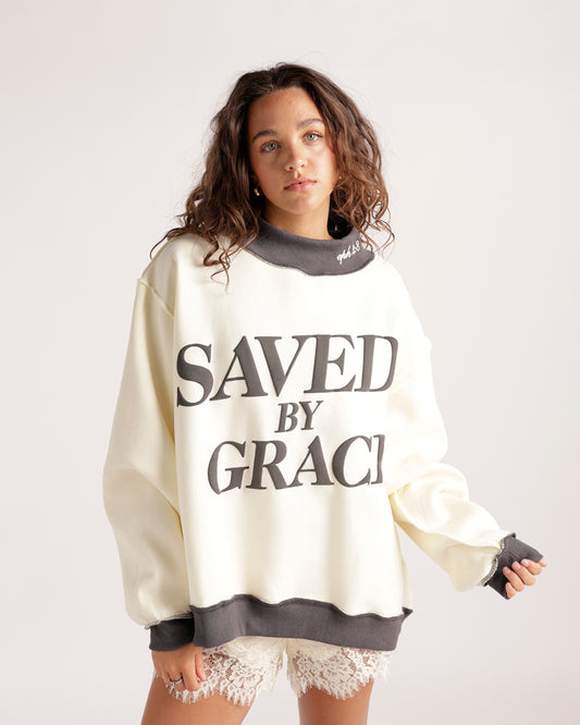 Explore comfort and style with this cream and dark grey colorblock sweatshirt. Features 'saved by grace' print, ombre wash, and a unique silhouette.