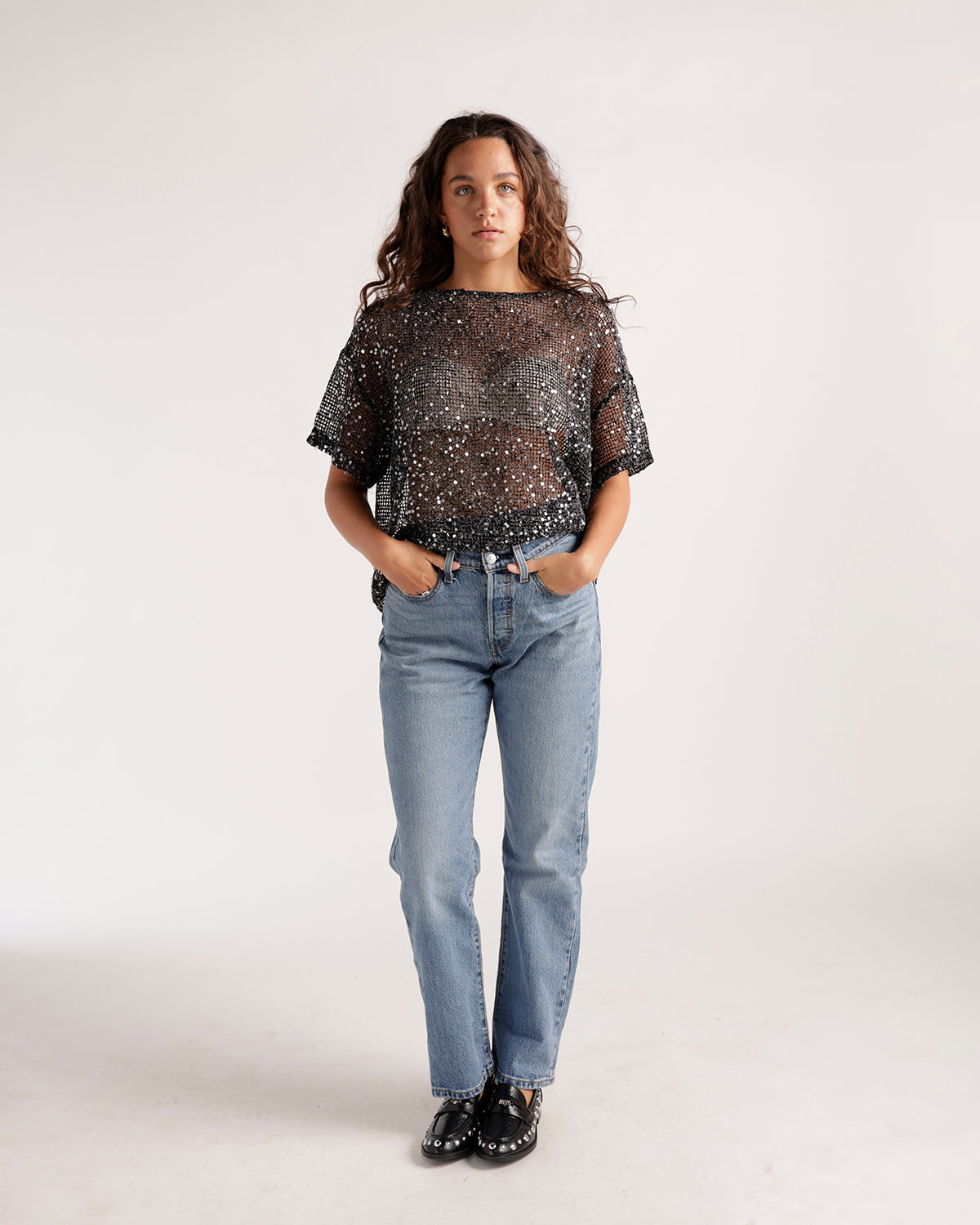 Light wash straight-leg jeans paired with sheer black sequin top and black loafers