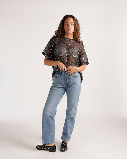 Light wash straight-leg jeans paired with a black sequin sheer top and black loafers