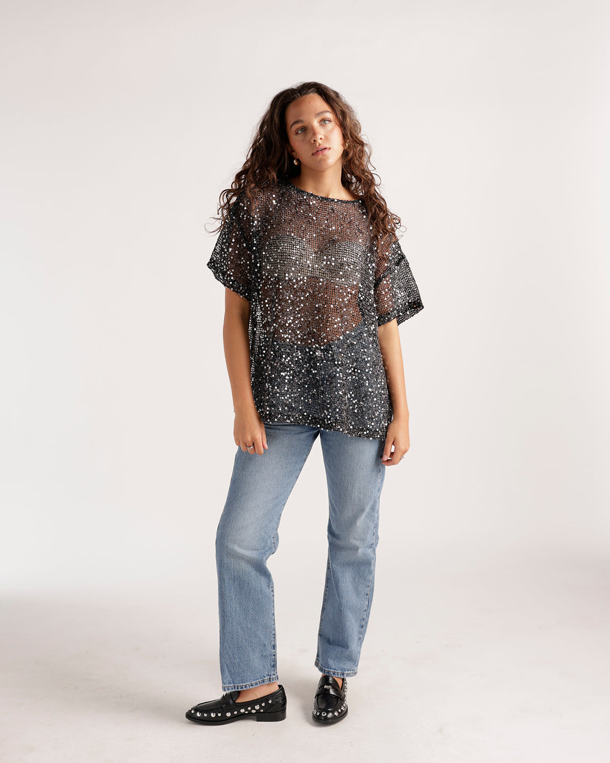 Light wash straight-leg jeans styled with a sheer black sequin oversized top and black loafers