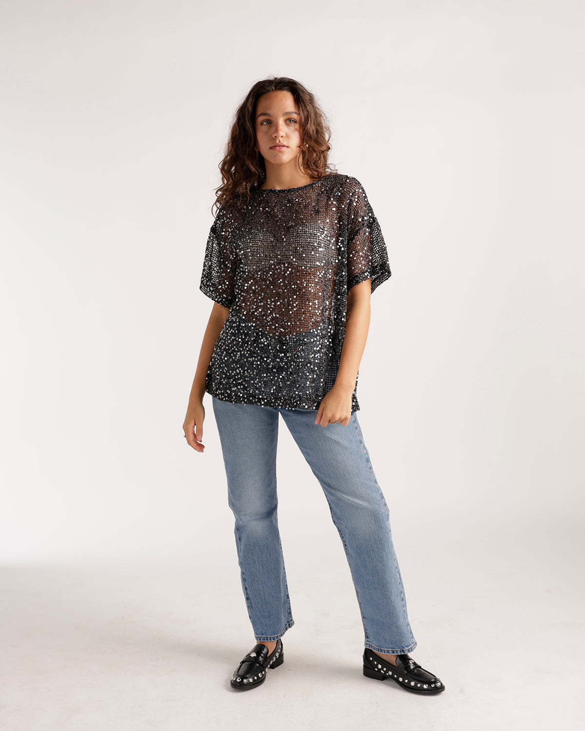 Light blue straight-leg denim jeans styled with a sheer sequin top and black loafers