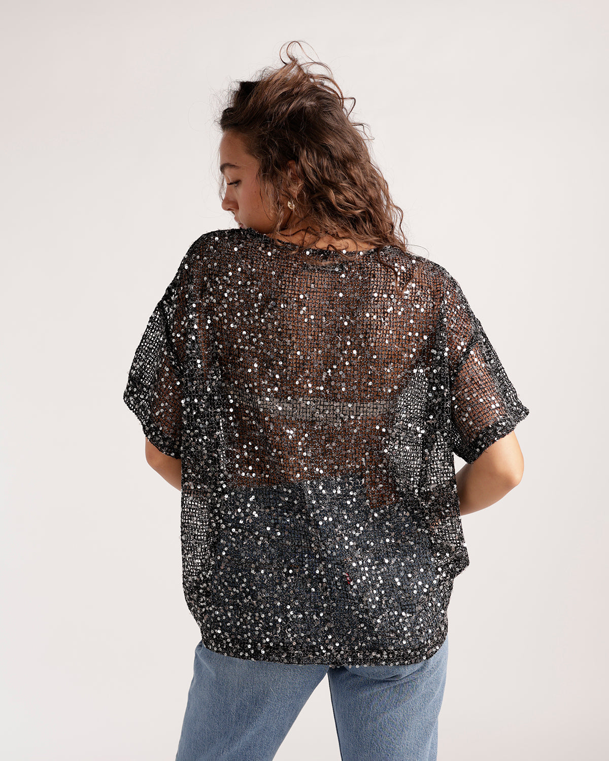 Black sheer sequin short sleeve top worn with blue jeans, back view