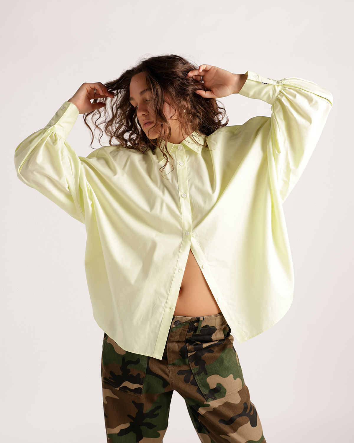Oversized pale yellow button-up shirt with wide sleeves, paired with camo pants.